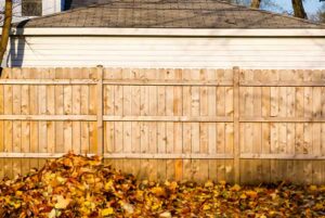 pile of fallen leaves against wood fence